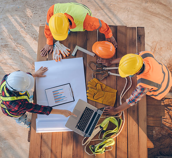 Construction workers in safety gear collaborating at Camelot HandyMan with a laptop and technical drawings.